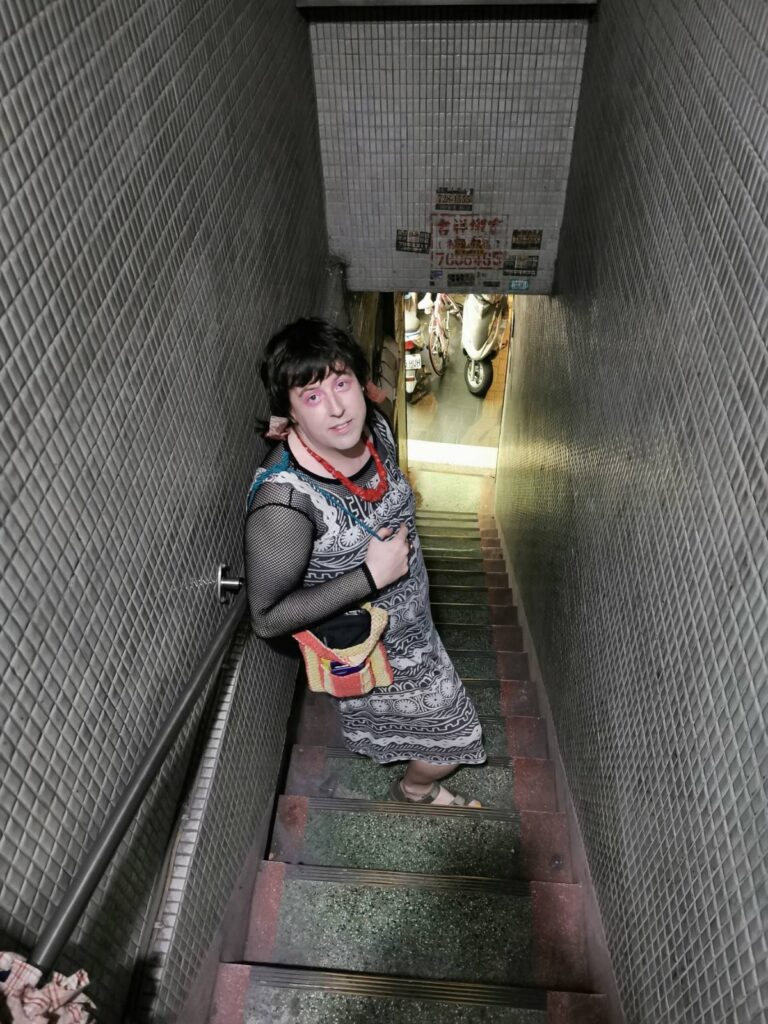 Lai standing in a tiled stairwell looking fab wearing a black and white dress and a red stone necklace.